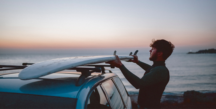 Surfista colocando la tabla de surf en la baca del coche
